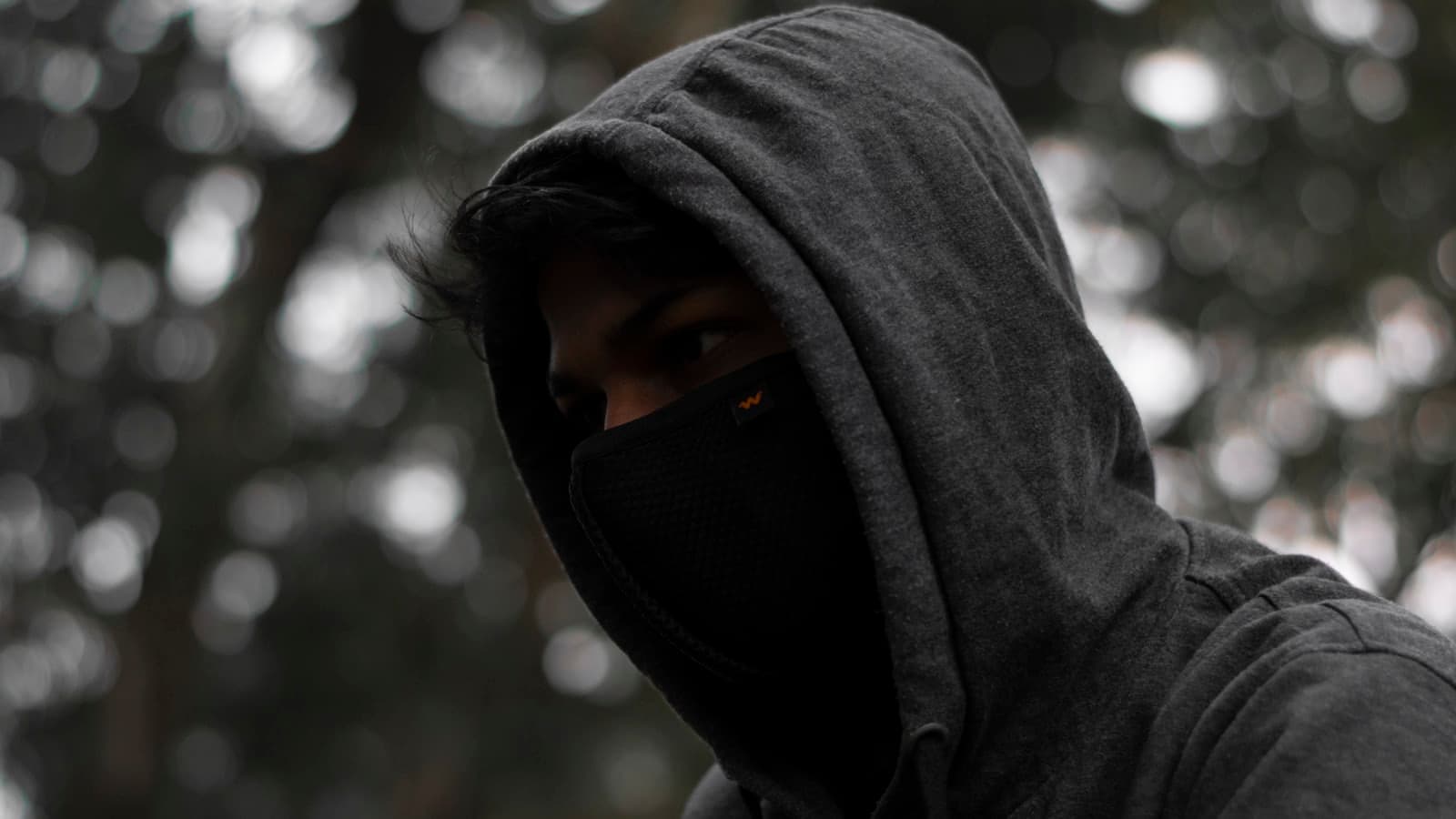 A person in a grey hooded top with their face covered by a dark mask